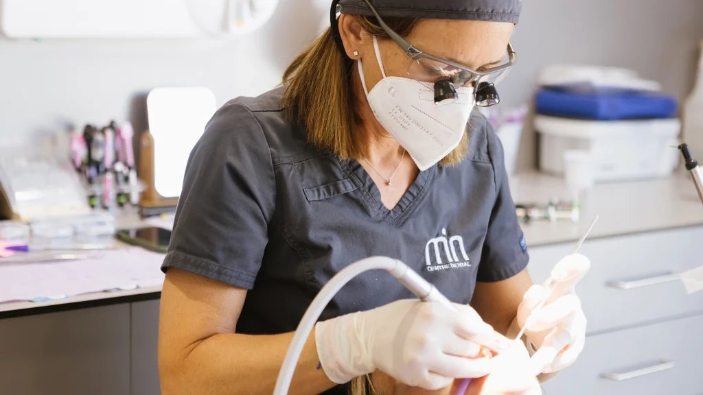 Professional de MiN Centre Dental atenent una pacient amb instrumental dental i ulleres d’augment.